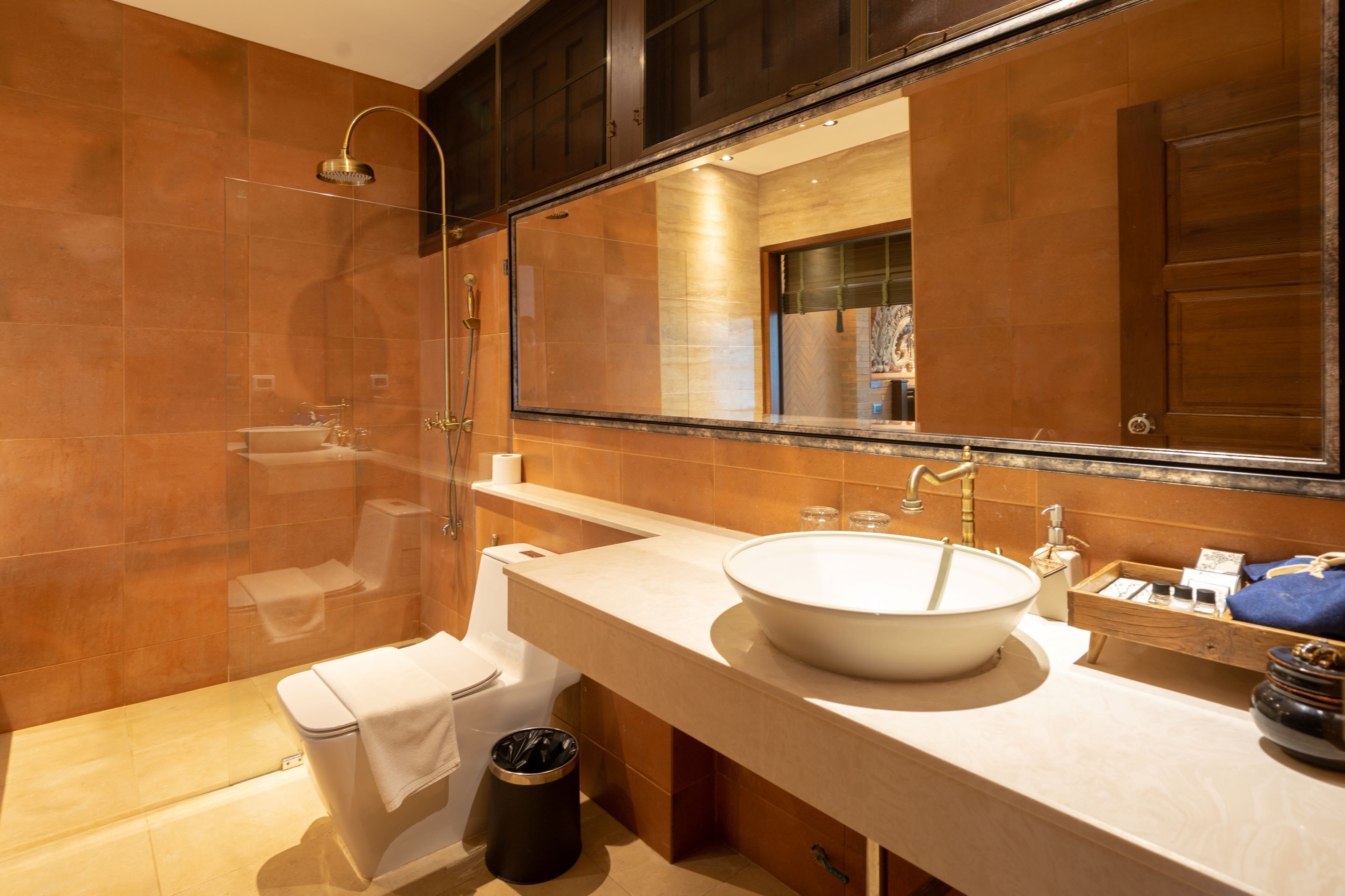 Un baño moderno con un espejo grande, un lavamanos blanco y una ducha con mampara de vidrio.