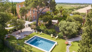 Una amplia piscina rectangular rodeada por un césped cuidado, una pared de piedra y una terraza de madera.