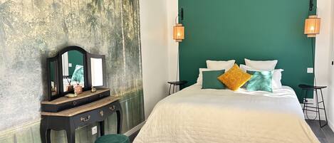 Een slaapkamer met een bed, een kaptafel, een spiegel, twee wandlampen en een groene accentmuur.