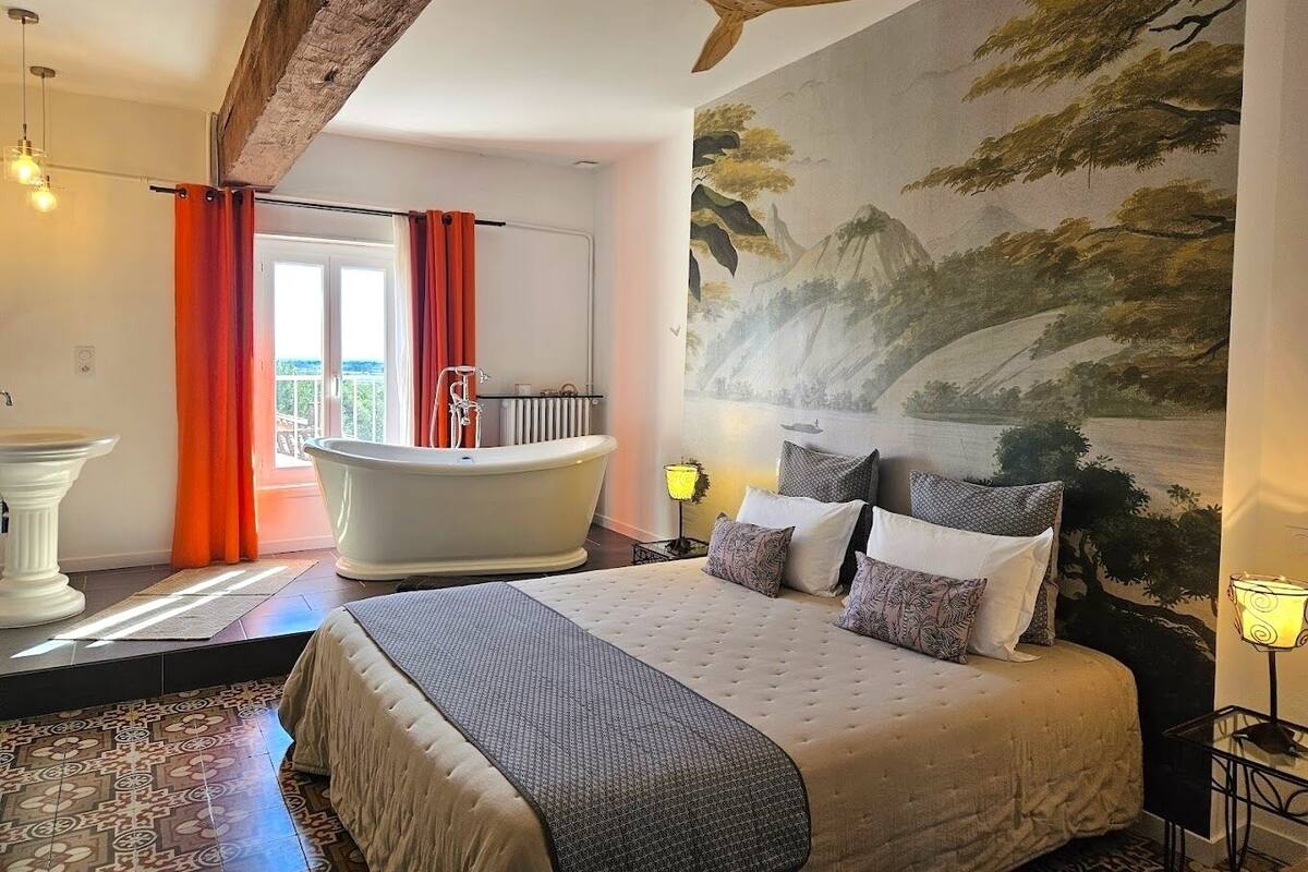 Ein Schlafzimmer mit einem großen Bett, einer Badewanne und einem Wandbild einer Landschaft.