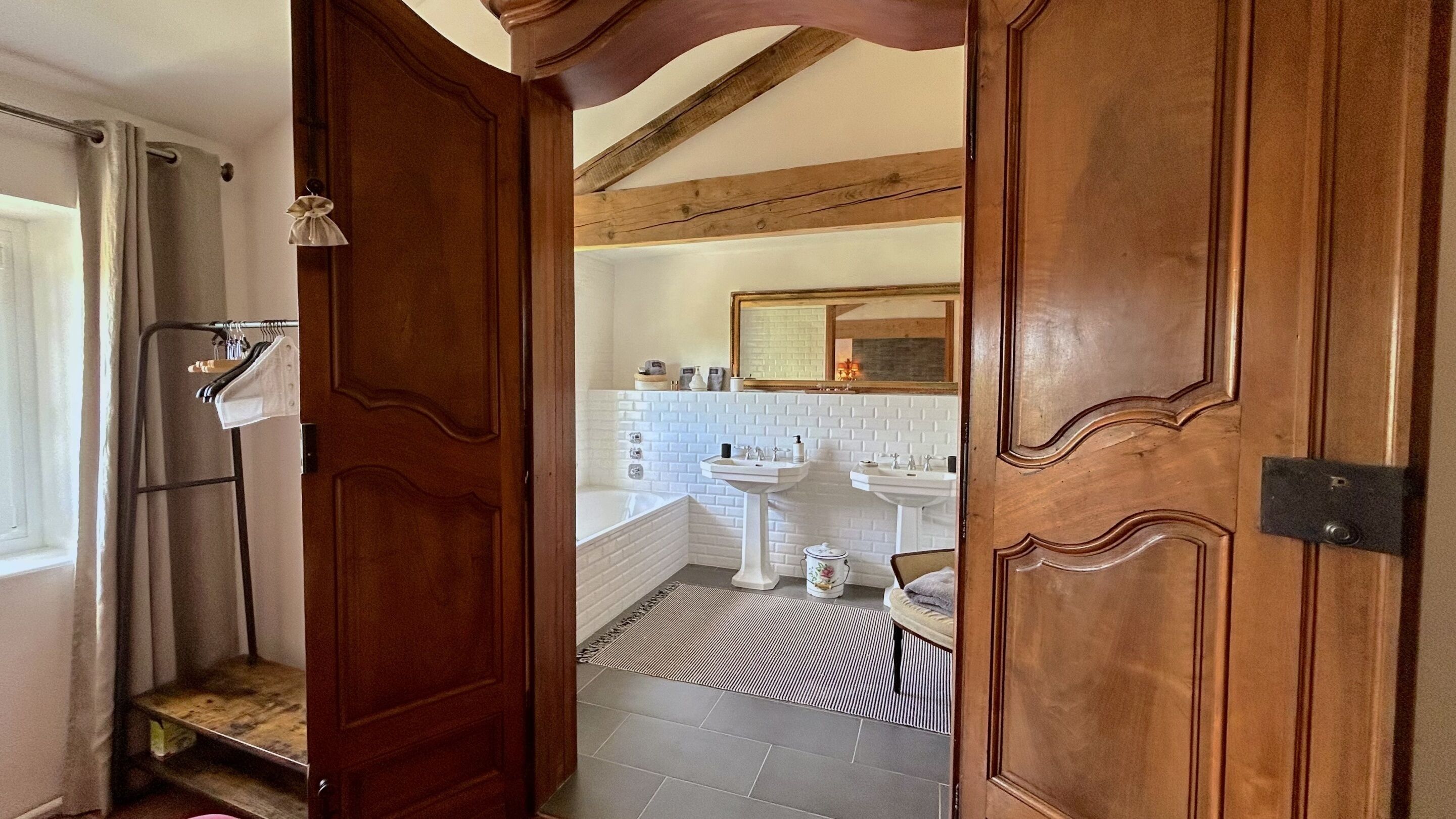 Puerta de madera que da a un baño con pared de azulejos blancos, un lavamanos y un espejo.