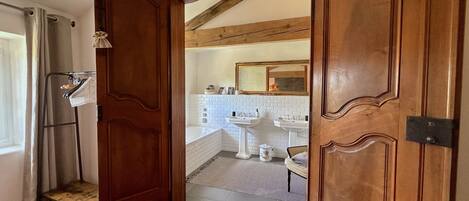 Puerta de madera que da a un baño con pared de azulejos blancos, un lavamanos y un espejo.