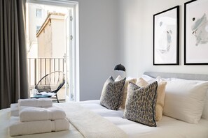 Une chambre d’hôtel avec un lit, deux coussins à motifs, une chaise et une fenêtre avec des rideaux.