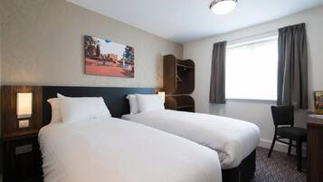Habitación de hotel con dos camas, un escritorio, una silla, un armario y una ventana con cortinas.