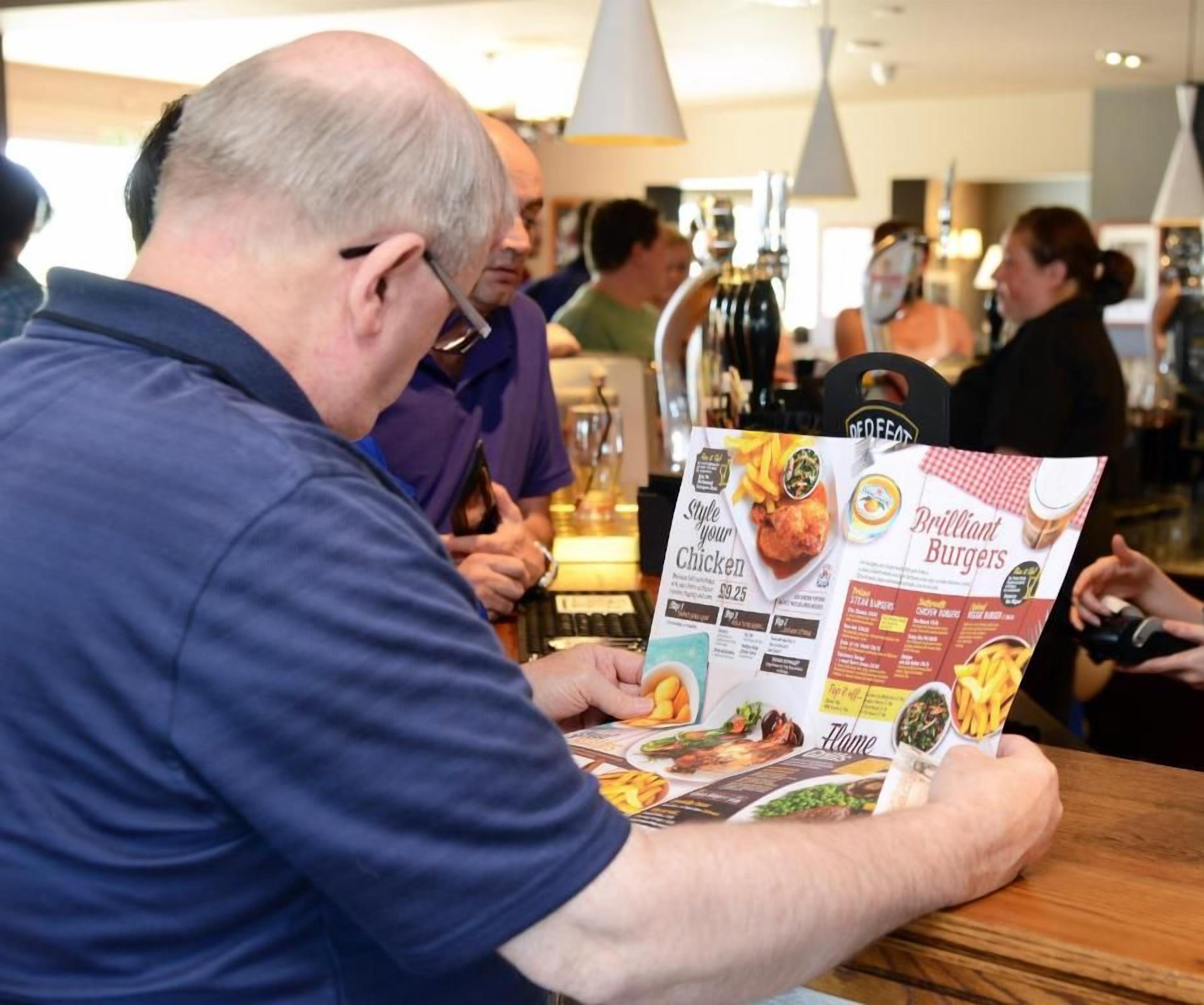 A person reading a menu at a restaurant with a bar in the background.
