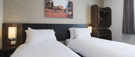 Una habitación de hotel con dos camas, una mesita de noche con lámpara, un armario y un cuadro en la pared.