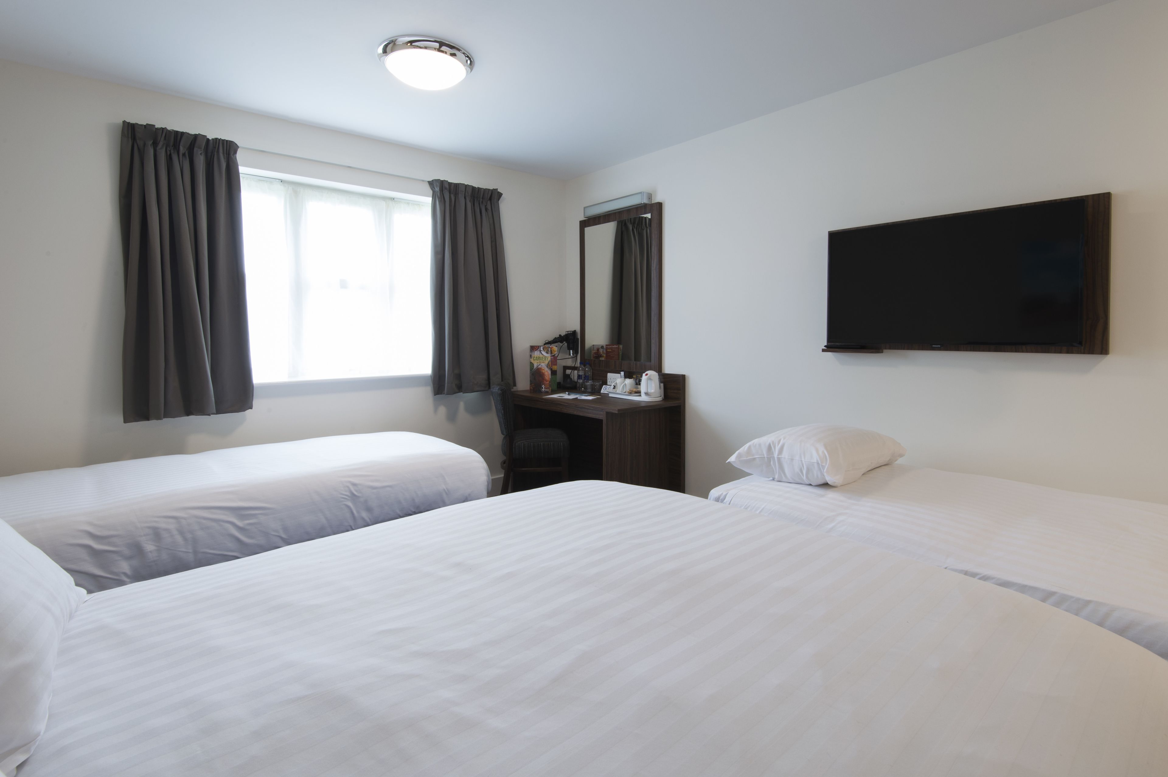 A hotel room with two beds, a desk, a mirror, and a TV.