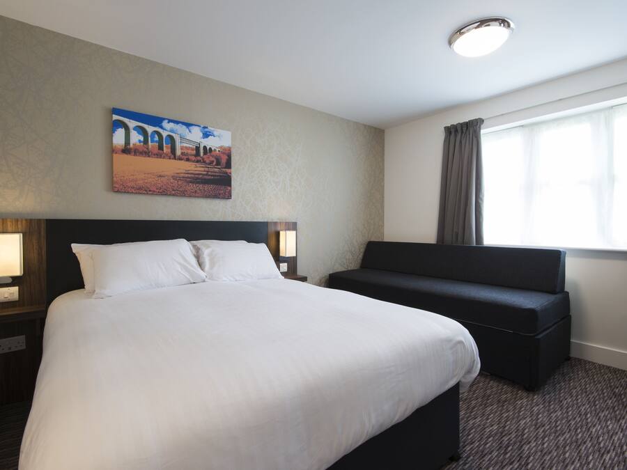 Ein Hotelzimmer mit einem großen Bett, einer Couch, einem Bild an der Wand und einem Fenster mit Vorhängen.