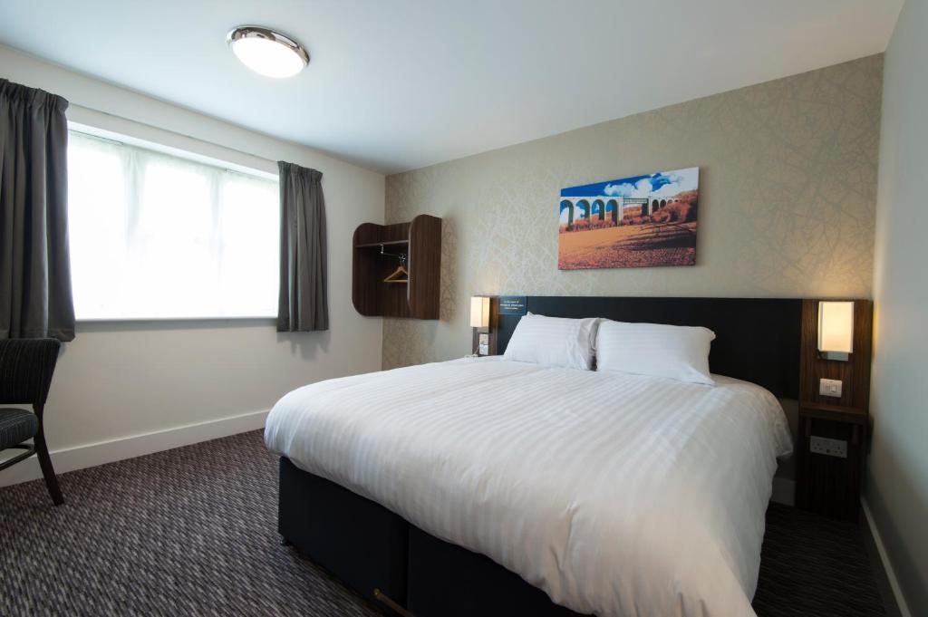 A hotel room with a large bed, a chair, a wall-mounted shelf, and a painting.