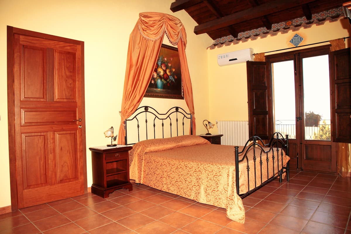 A bedroom with a bed, nightstands, a wooden door, and a window with curtains.