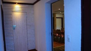 Ein Korridor mit einer Holztür und einer Glastür, die in einen Essbereich mit Stühlen führt.
