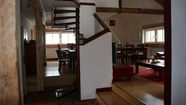 Ein geräumiges Wohnzimmer mit einer Holztreppe, eine Essecke mit Stühlen und einem Tisch sowie eine Küche im Hintergrund.