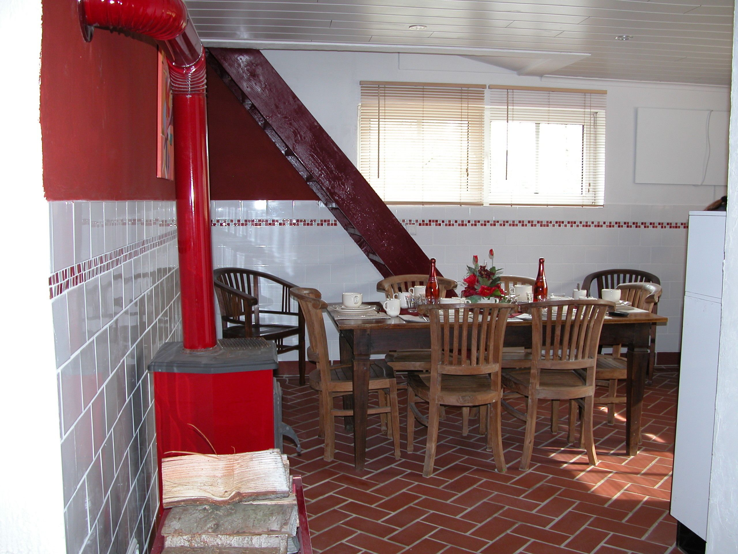 A dining area with a brick floor, wooden chairs, a table set for four, and a red staircase leading to an upper level.