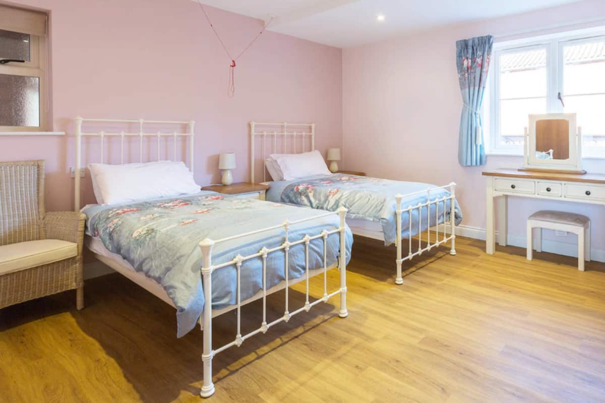 A bedroom with two beds, a wooden desk, a chair, and a window with curtains.