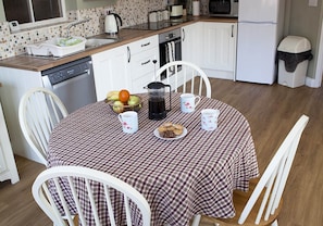 A small kitchen with white cabinets, a dishwasher, and a coffee maker on the counter. - Damerons Farm Cottages (Ipswich)