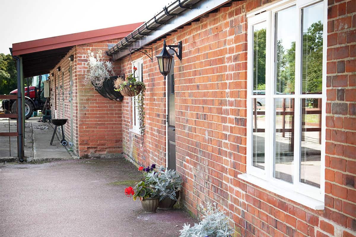 A brick building with a red roof, large windows, and hanging flower baskets.
