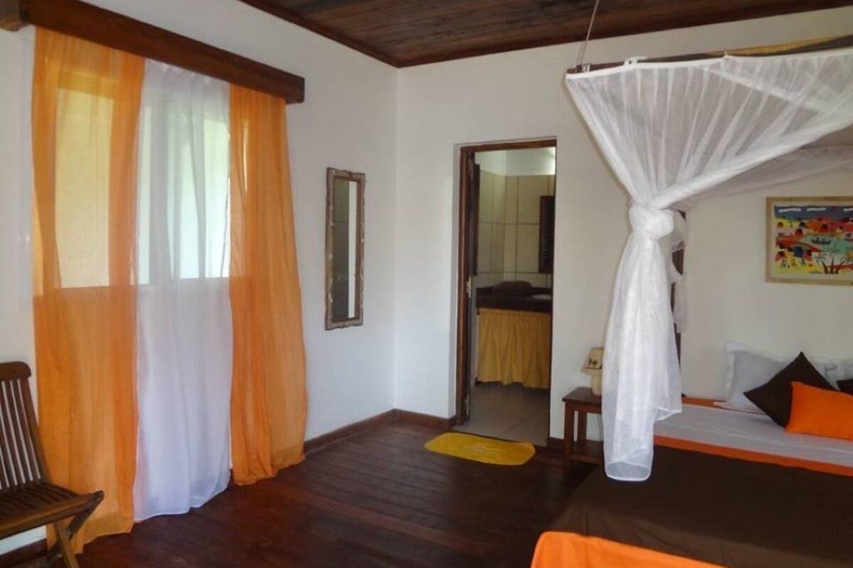 A bedroom with a bed, a chair, a mosquito net, and a door leading to another room.