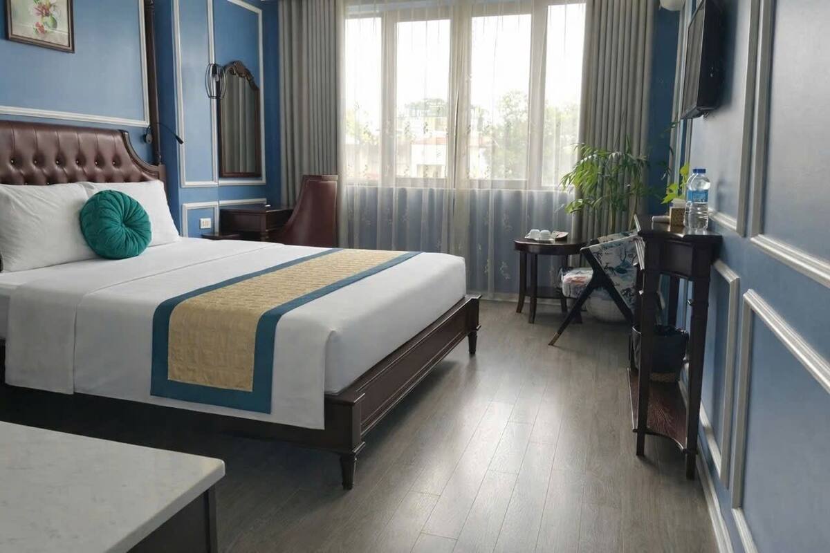 A hotel room with a large bed, a desk, a chair, and a TV on the wall.
