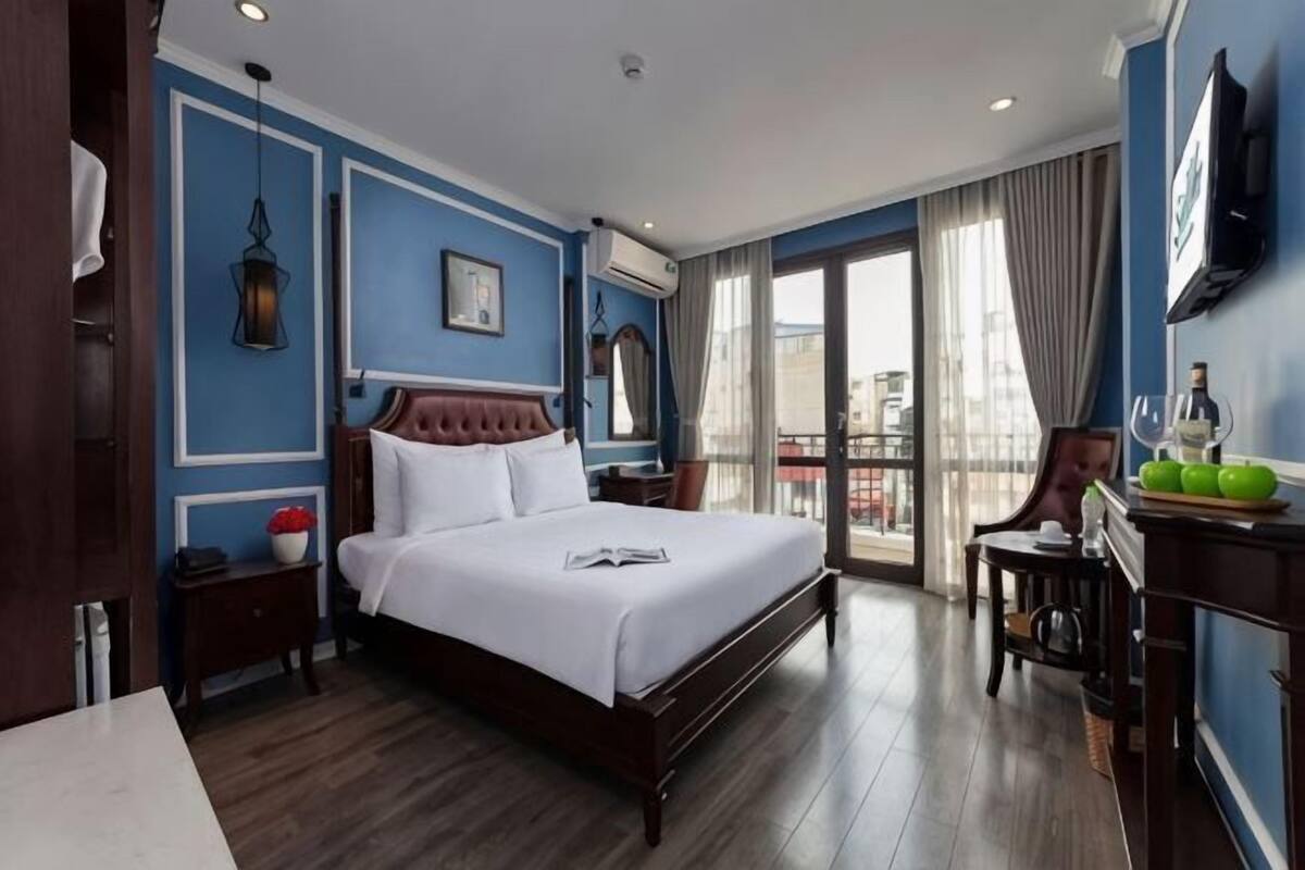 A hotel room with a large bed, a desk, a chair, a window with a view, and a balcony.