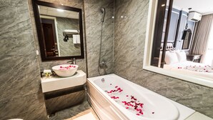Une salle de bain moderne avec un mur en marbre, une grande baignoire remplie de pétales de rose, un lavabo et un miroir.
