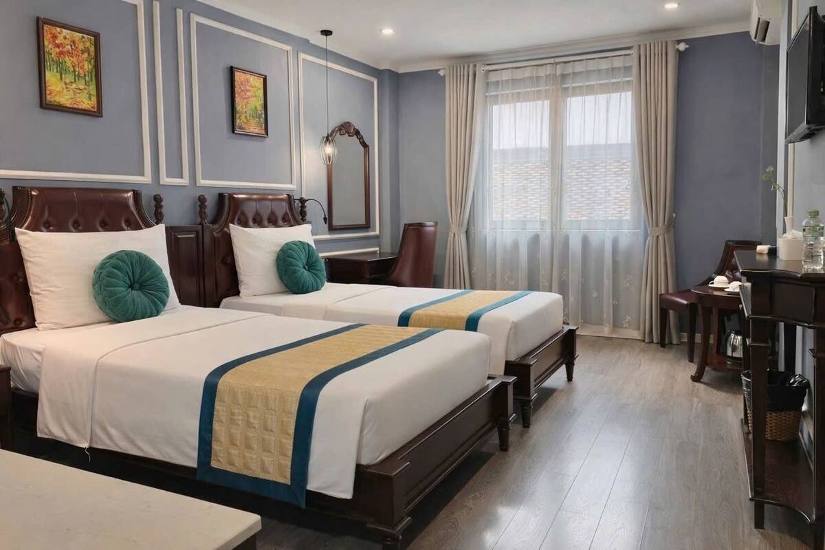 A hotel room with two beds, a desk, a chair, a TV, and a large window with curtains.