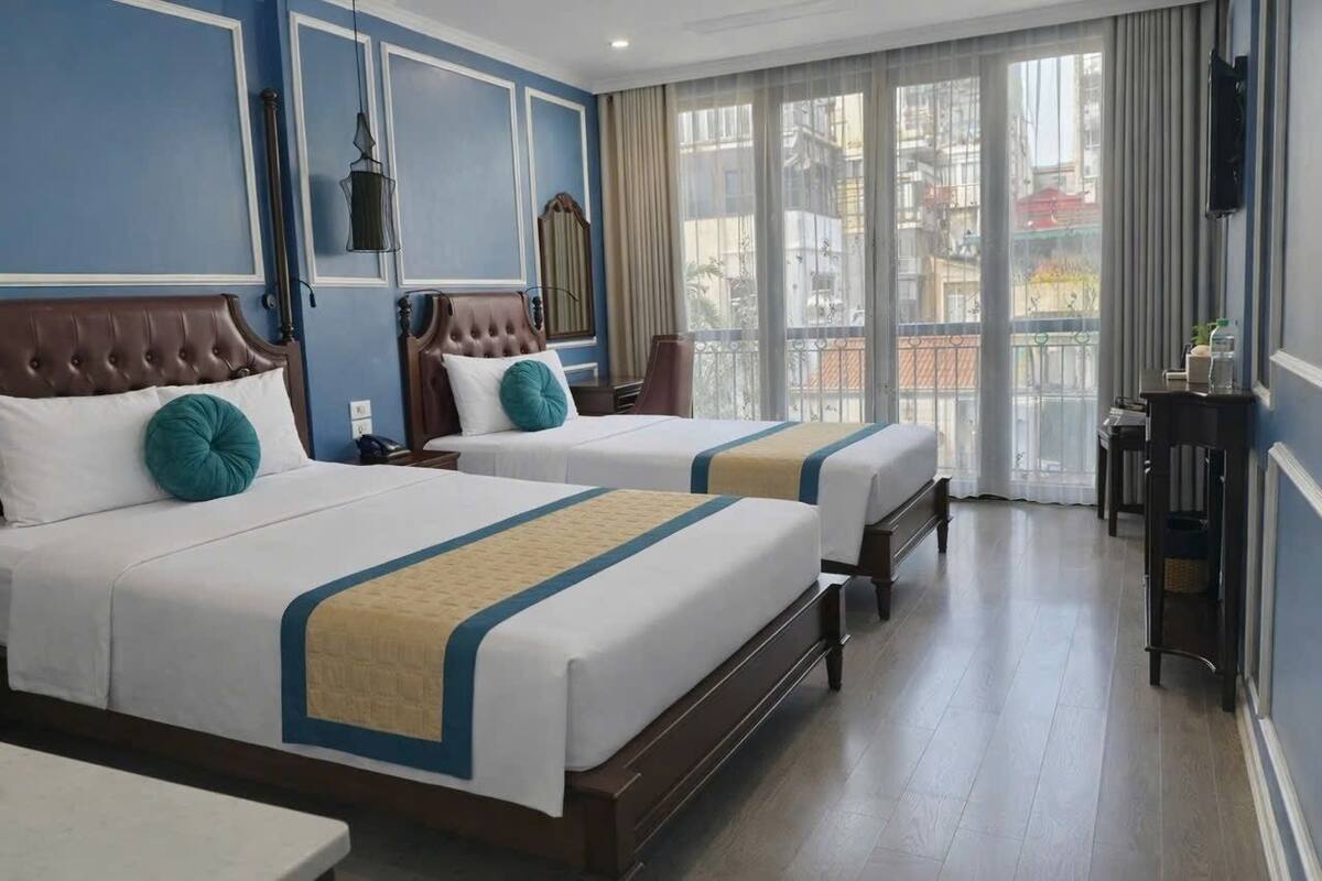 A hotel room with two beds, a large window with a view, a small table, and a TV mounted on the wall.