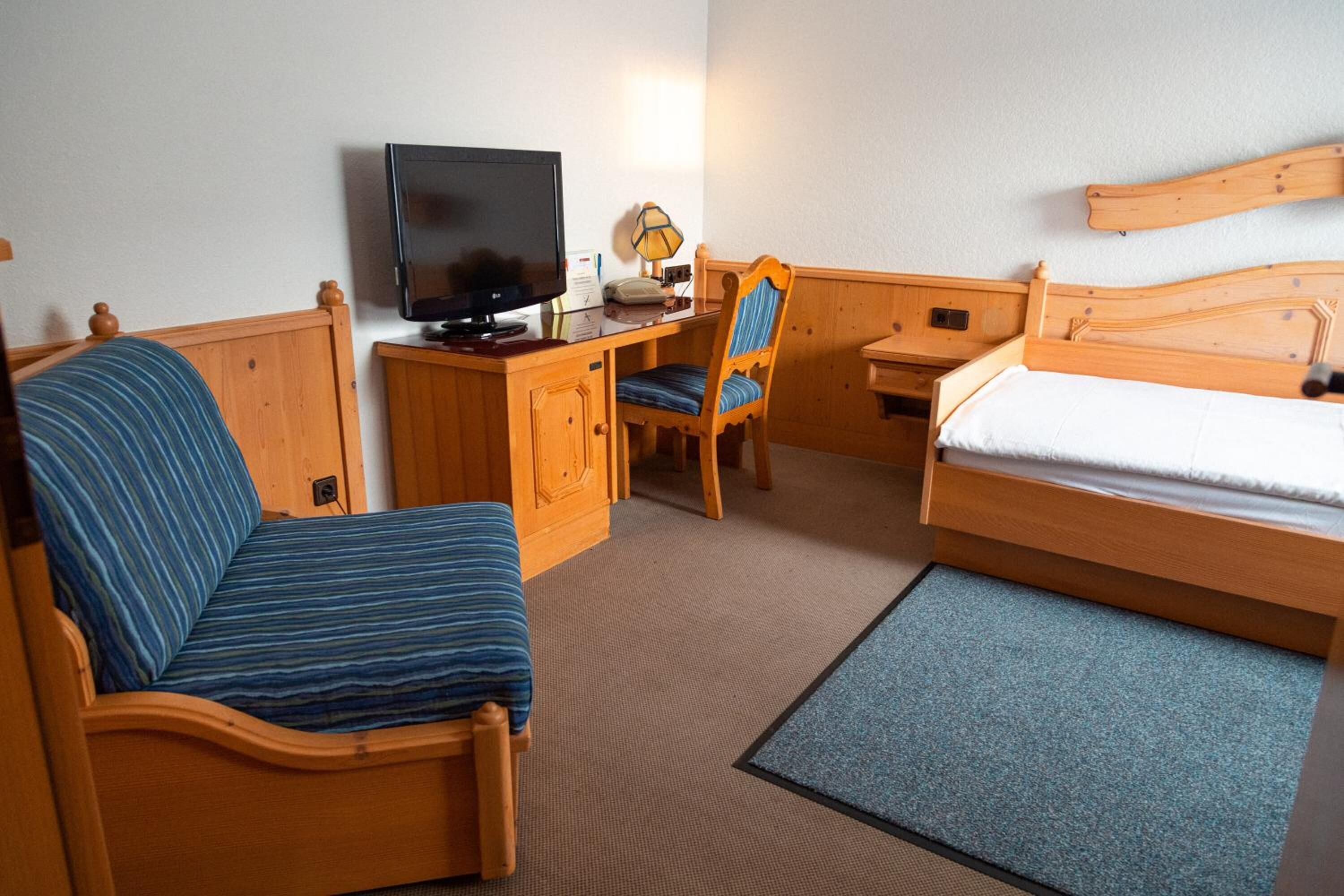 A hotel room with a bed, a desk with a television, a chair, and a small table.