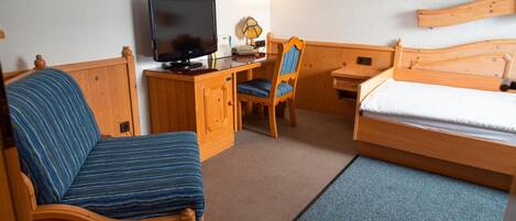 A hotel room with a bed, a desk with a television, a chair, and a small table.