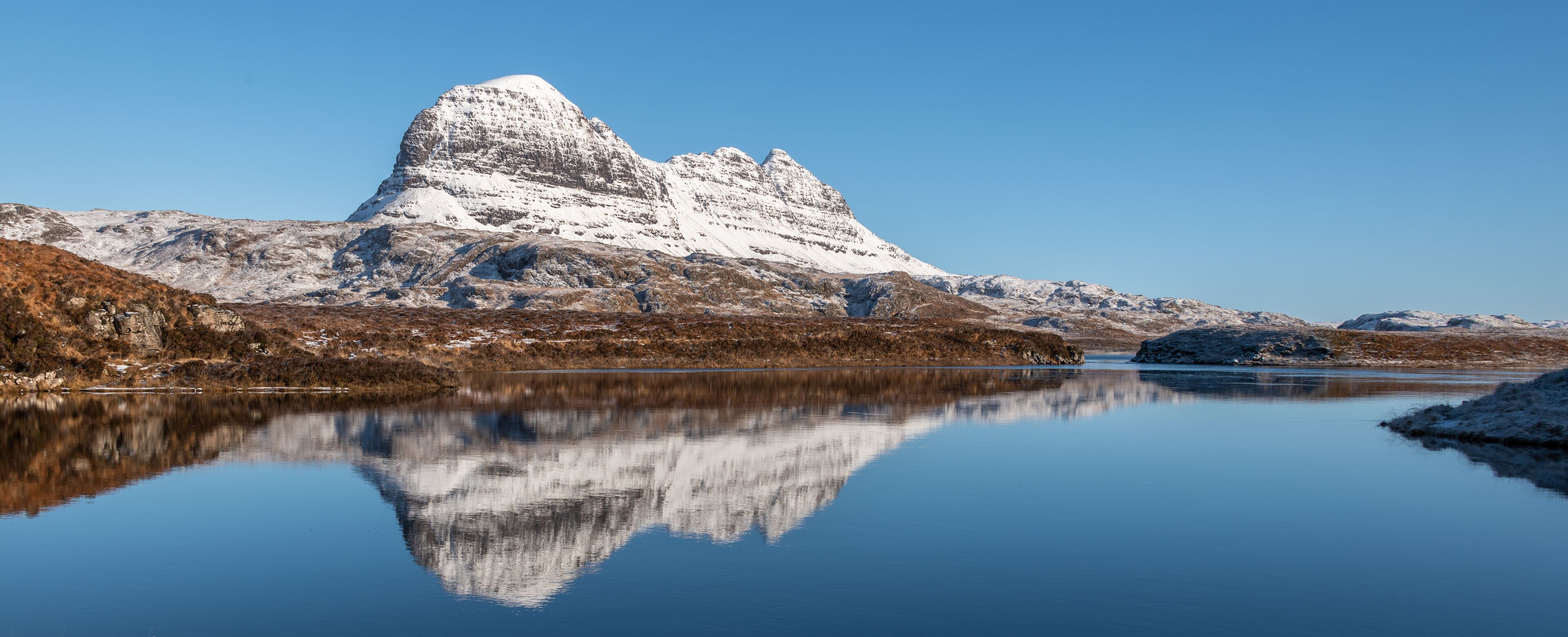 Una montaña con cima nevada reflejada en un lago tranquilo.