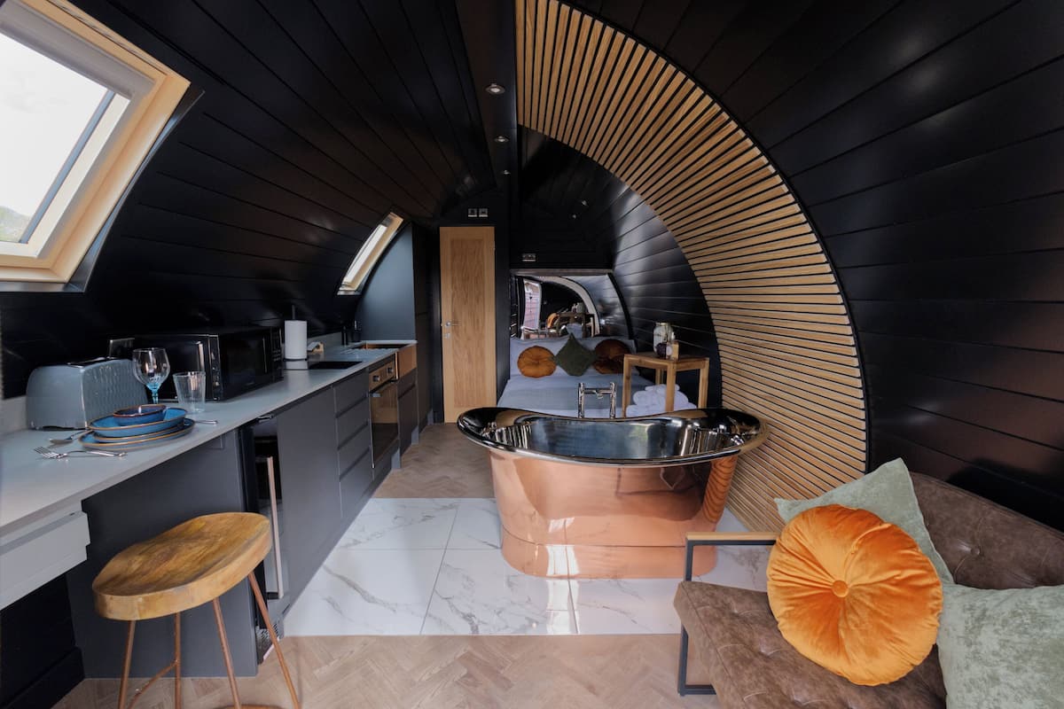 A compact, modern kitchen with a large copper sink, a wooden stool, and a dining area with a table and chairs.