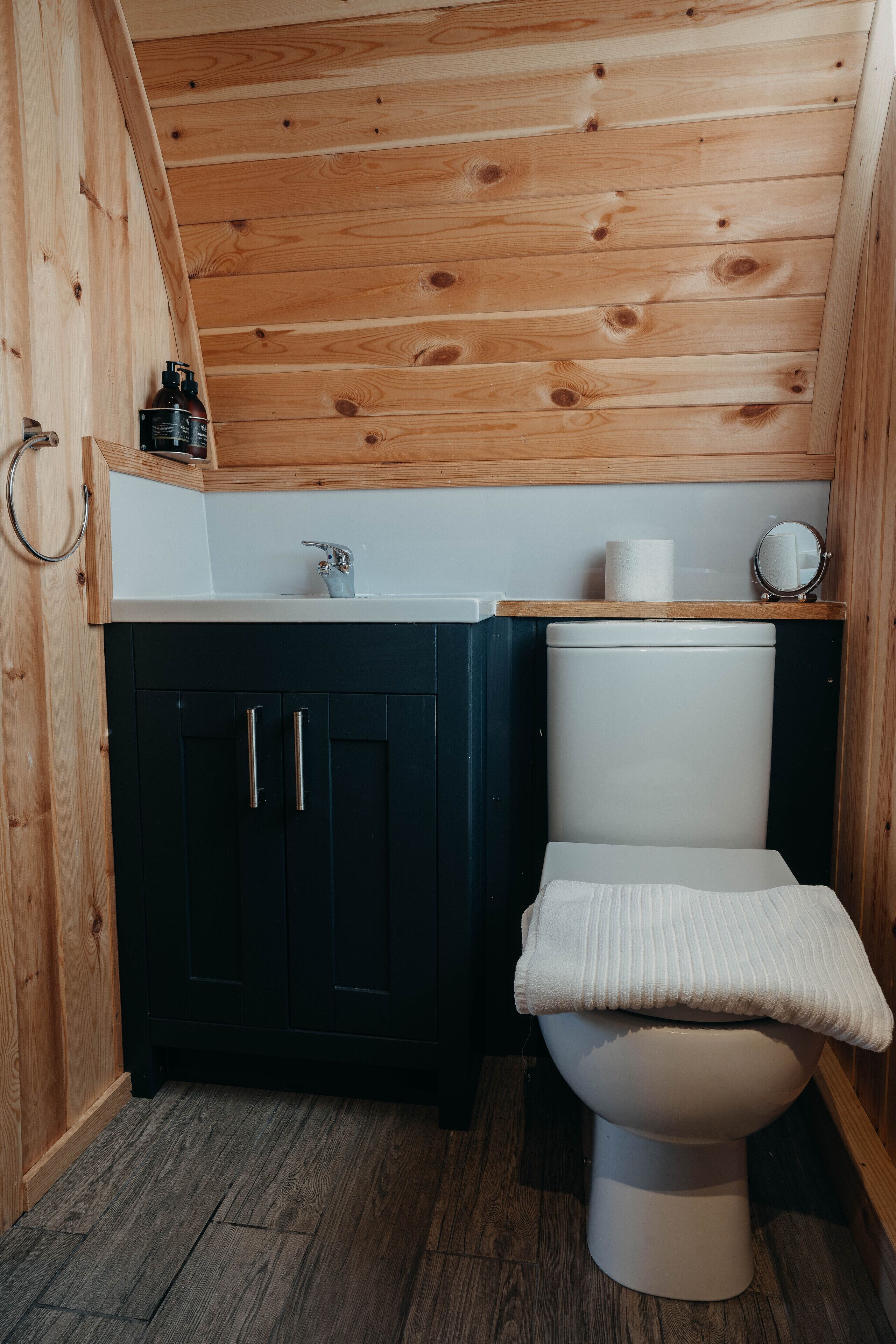 A compact bathroom with a wooden ceiling, a white toilet, and dark cabinets.