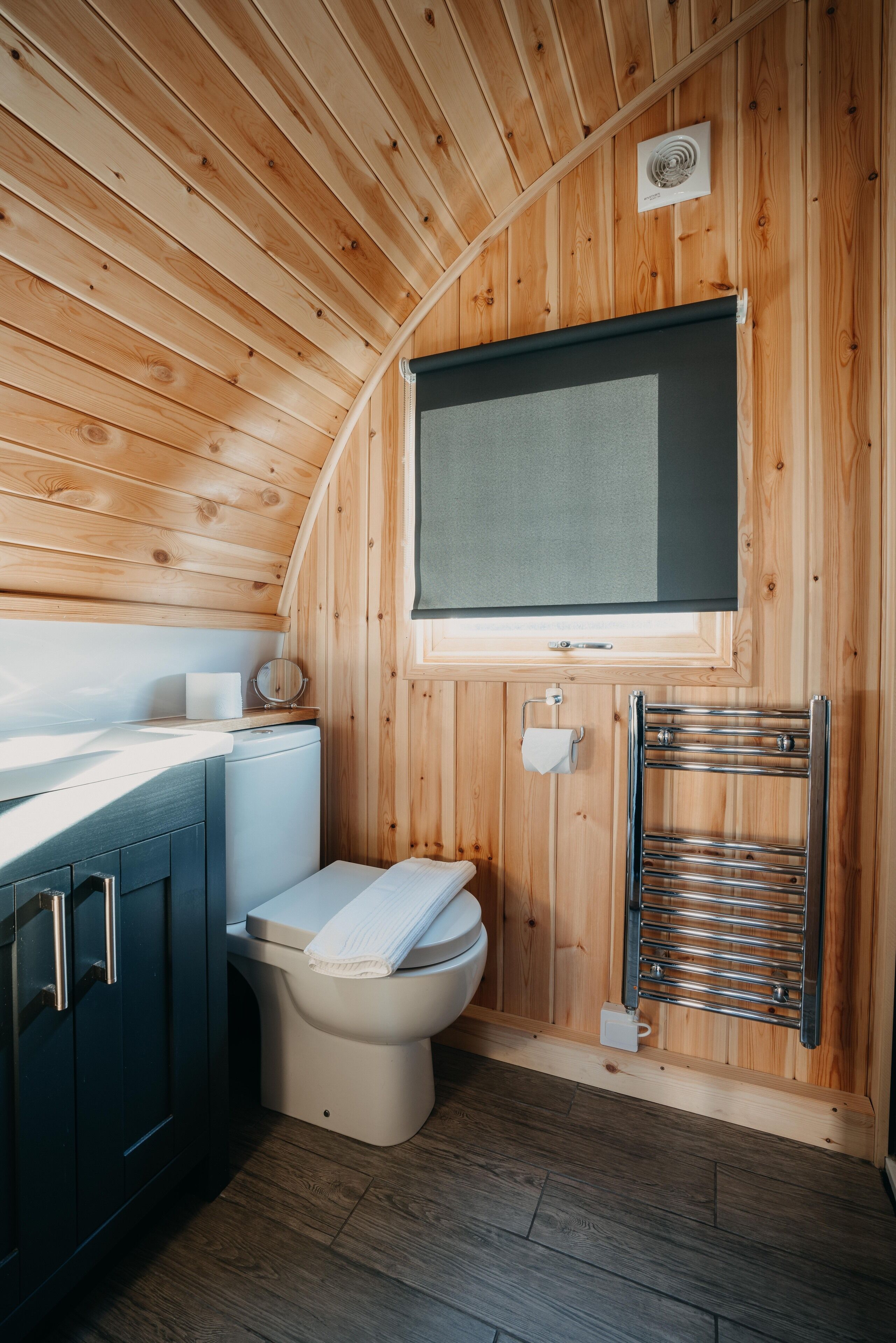 A compact wooden cabin bathroom with a toilet, sink, and a towel rack.