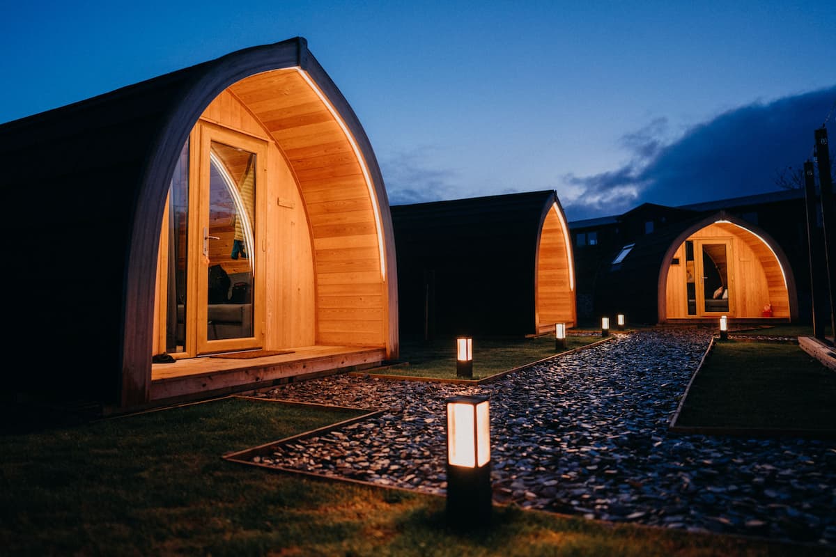 A row of wooden pod-style cabins with large windows and a gravel pathway leading to them.