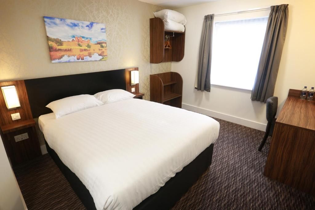 Une chambre d’hôtel avec un grand lit, un bureau, une chaise, une armoire et un tableau au mur.
