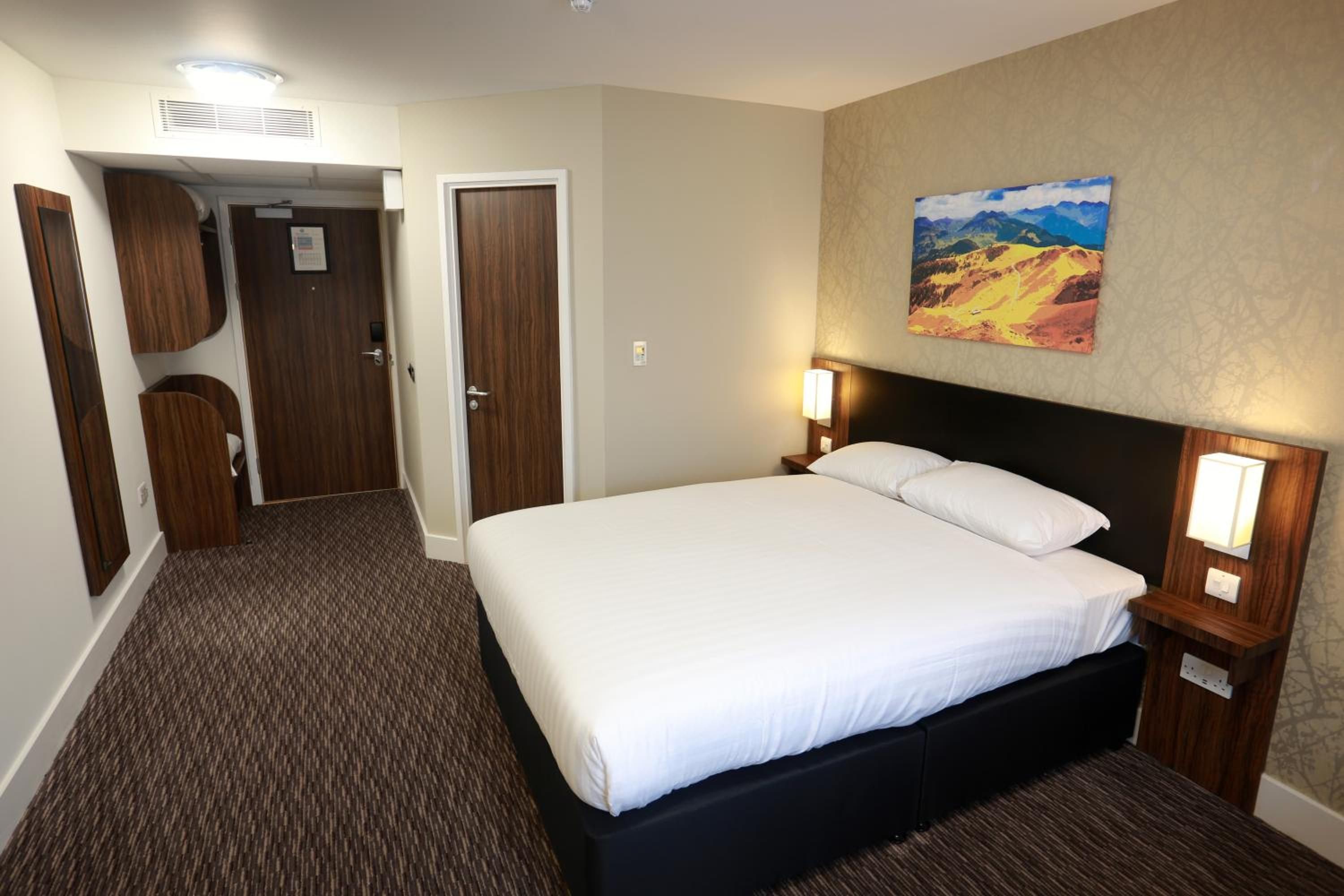 A hotel room with a large bed, a painting on the wall, and a carpeted floor.
