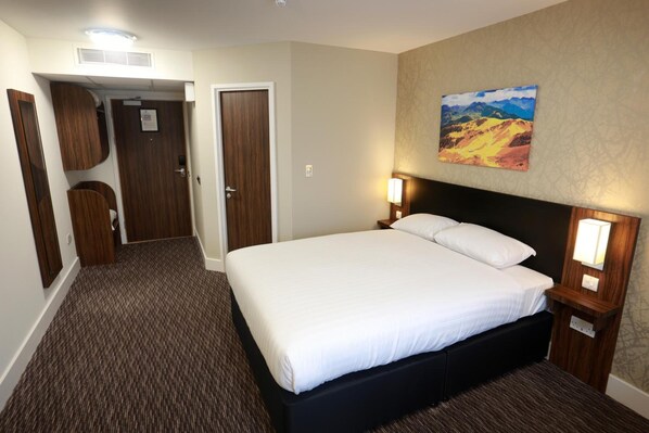 A hotel room with a large bed, a painting on the wall, and a carpeted floor.