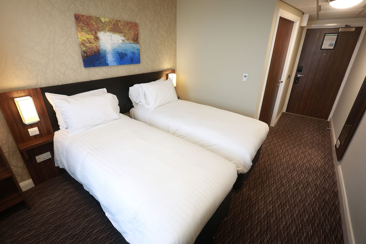 A hotel room with two beds, a painting on the wall, and a carpeted floor.