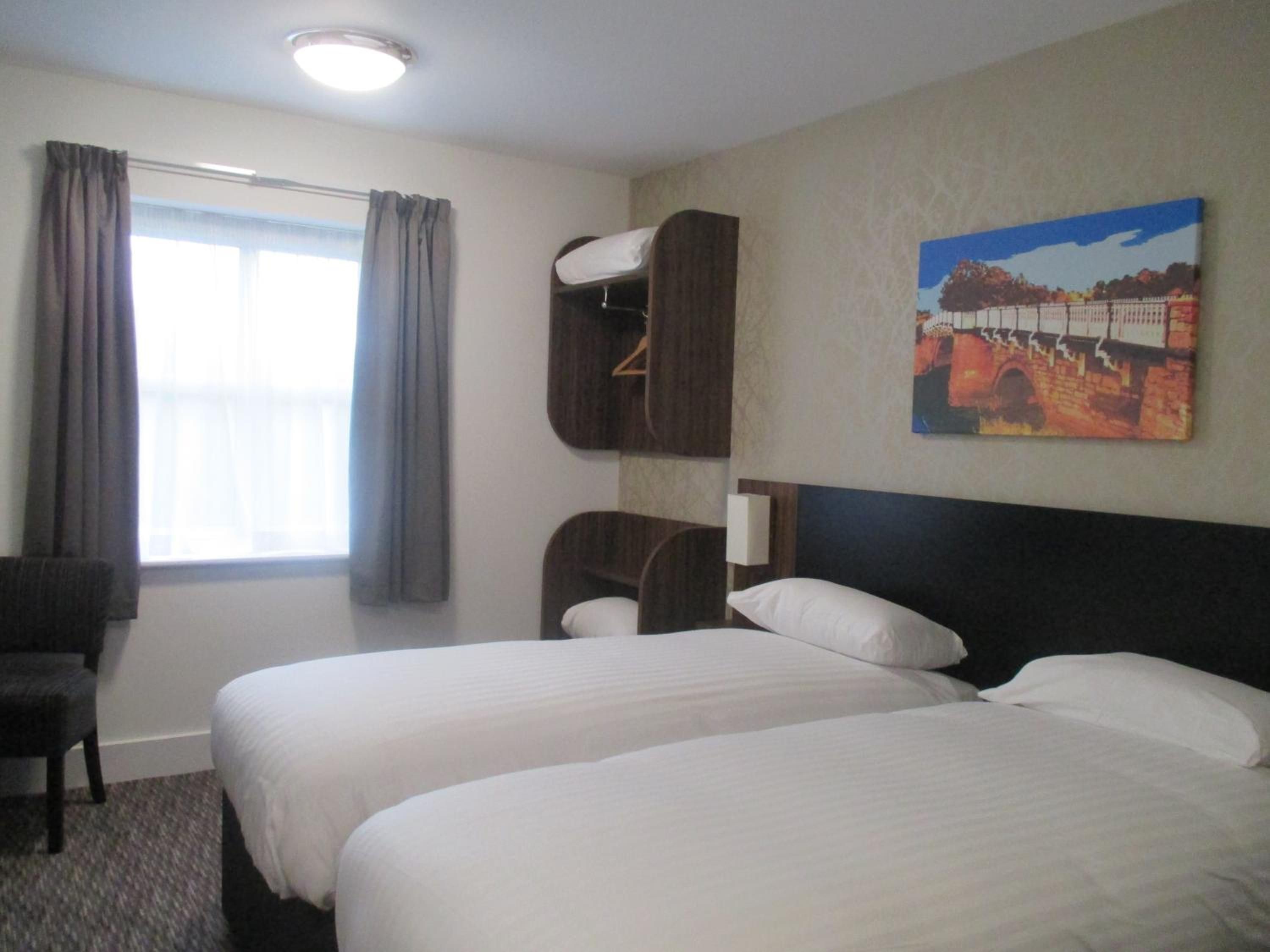 A hotel room with two beds, a chair, a painting on the wall, and a window with curtains.