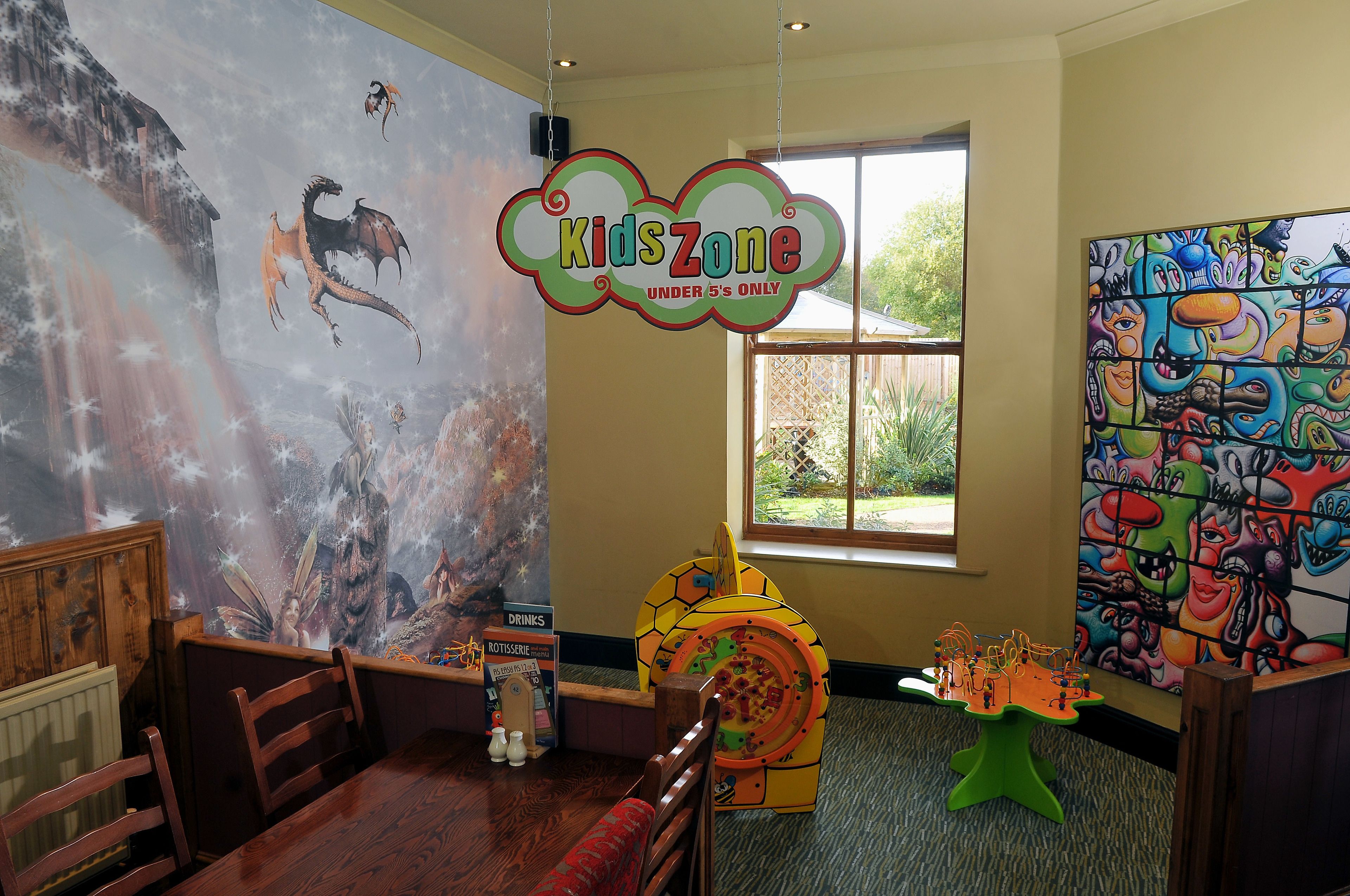Un área de juegos infantiles con un mural, una estructura de juego temática de pizza y un letrero que indica que es para niños menores de 5 años.