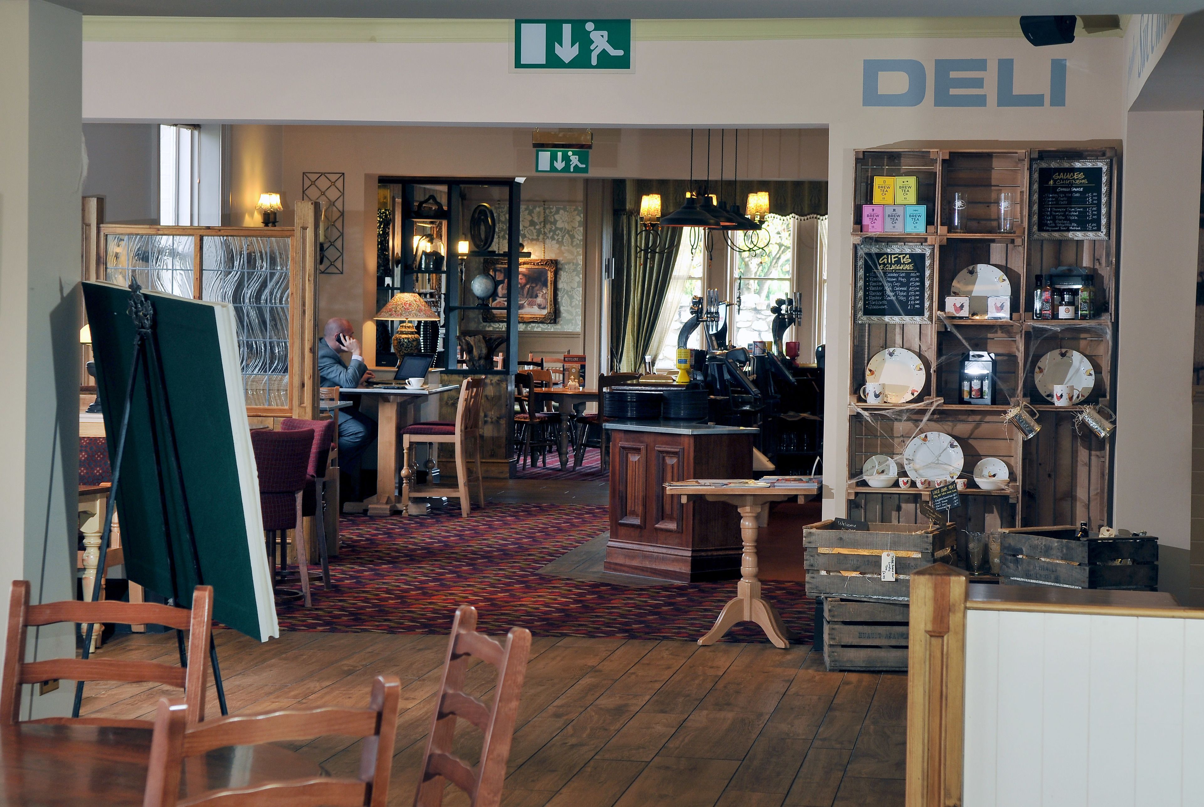 A cozy cafe interior with wooden furniture, a chalkboard menu, and a green exit sign.