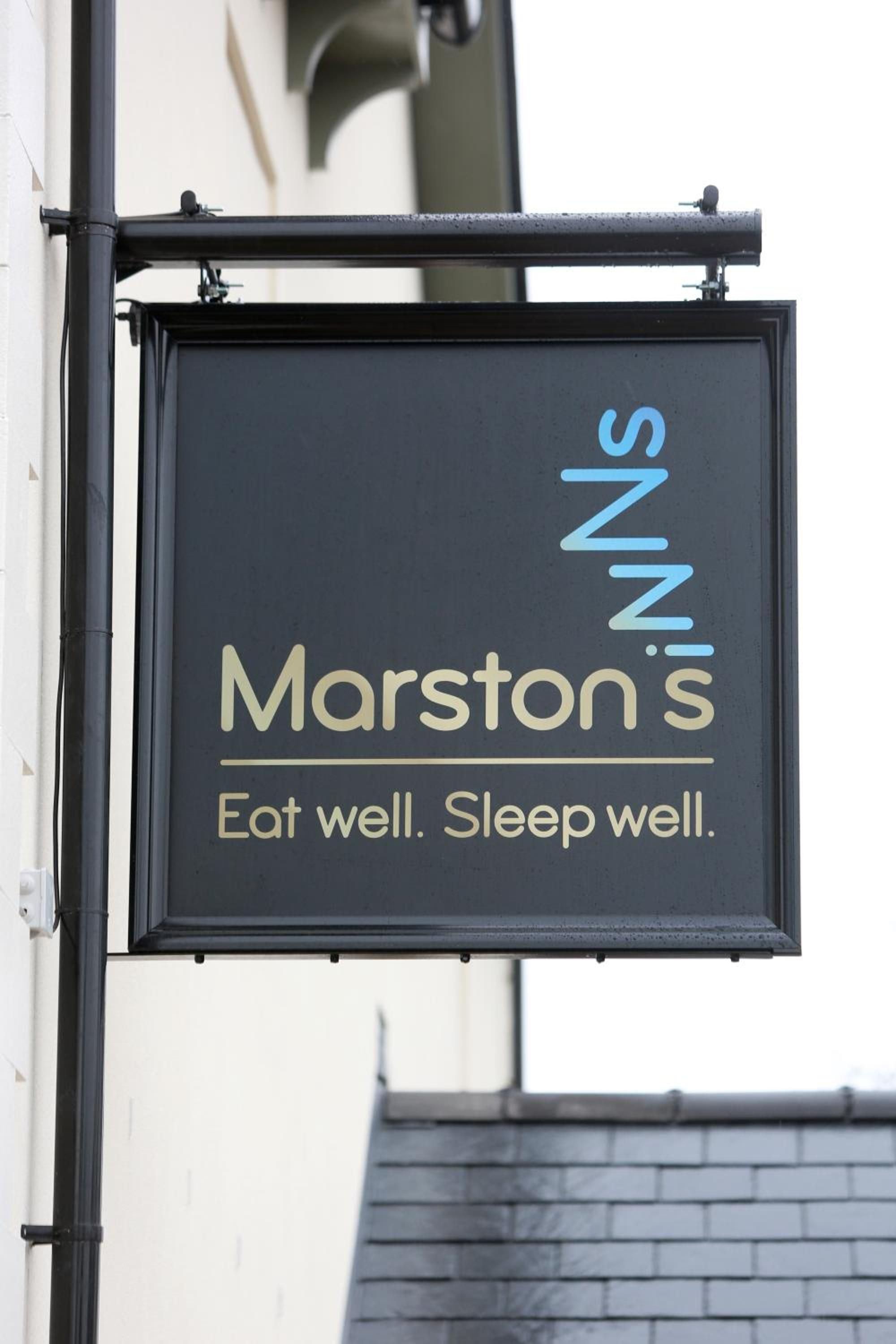 Un letrero negro con letras doradas que dice 'Marston's' y el lema 'Come bien. Duerme bien.'