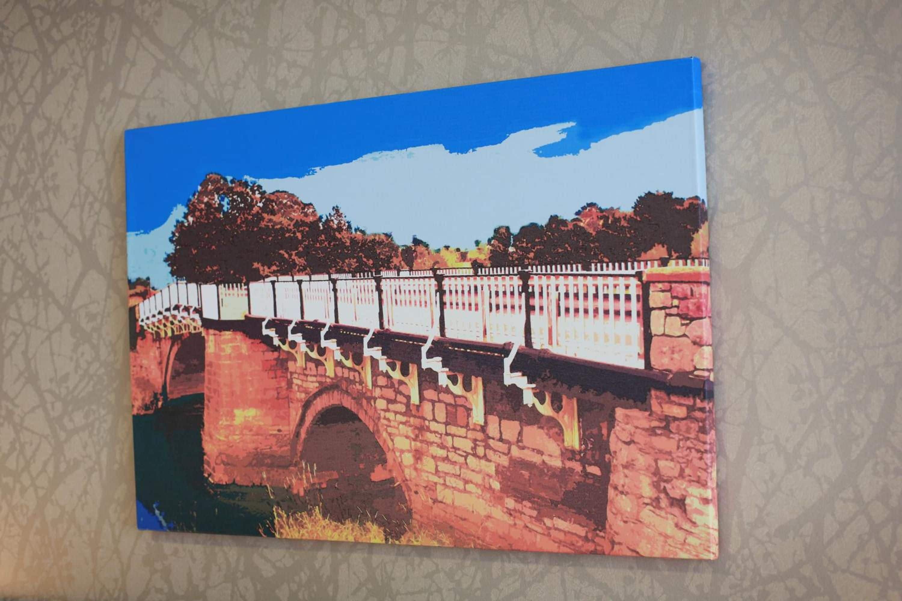 A painting of a stone bridge with a white railing, set against a backdrop of trees and a clear sky.