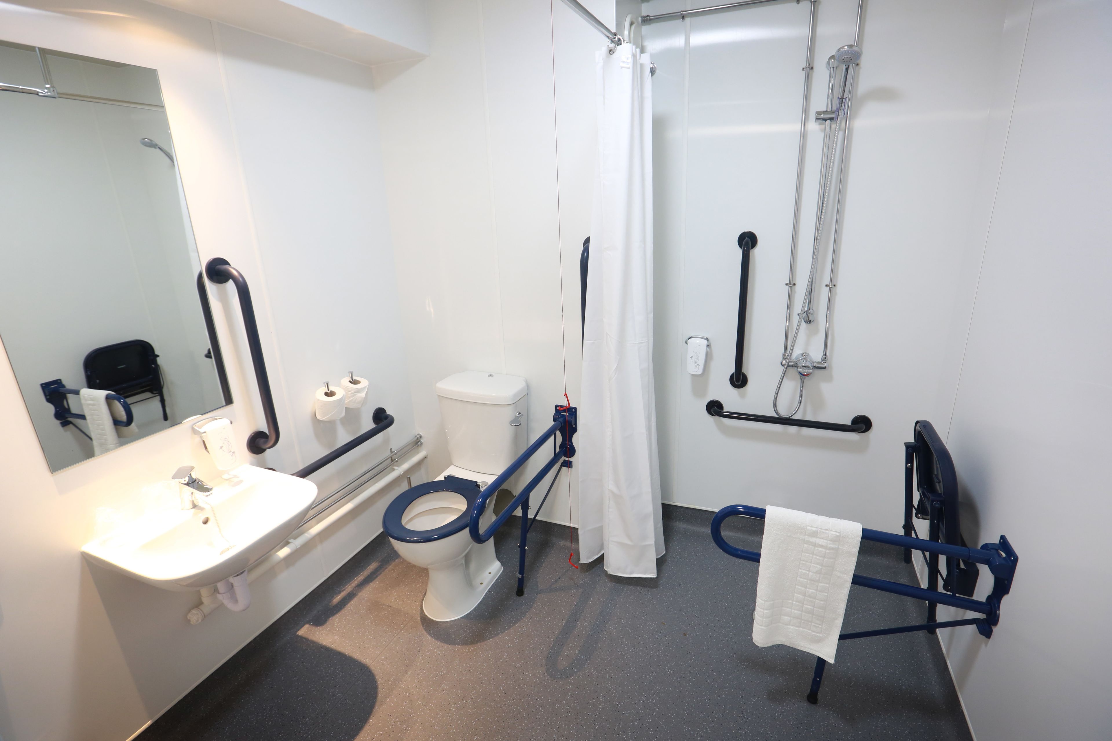 Une salle de bain avec un lavabo blanc, des toilettes, une douche avec un rideau blanc et un porte-serviettes.