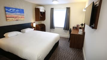 A hotel room with a large bed, a desk with a mirror, a window with curtains, and a painting on the wall.