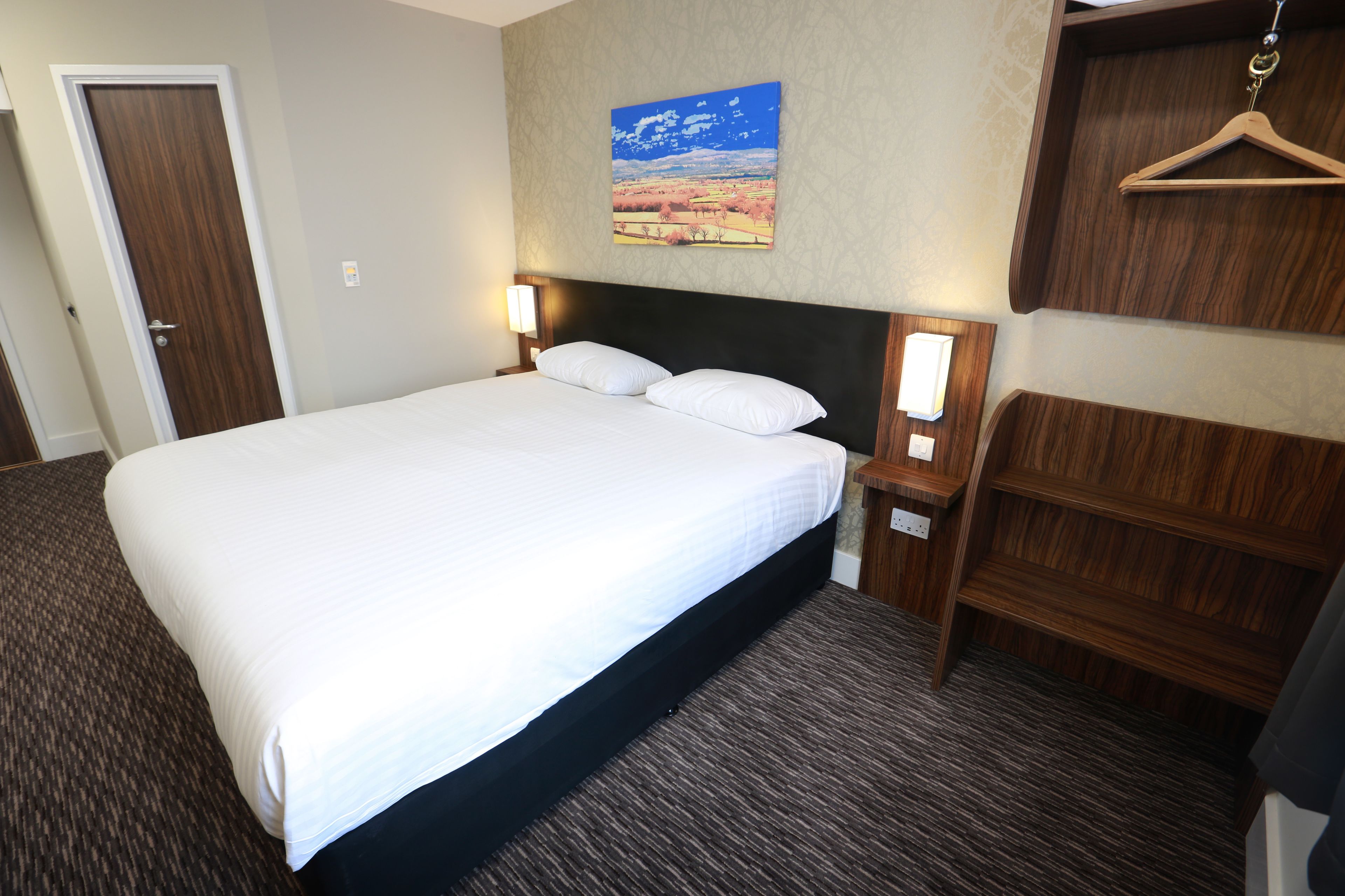 Habitación de hotel con una cama grande, dos mesitas de noche con lámparas, un cabecero de madera, un armario de madera y un cuadro en la pared.