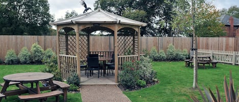 A wooden gazebo with a bench and picnic table in a backyard.