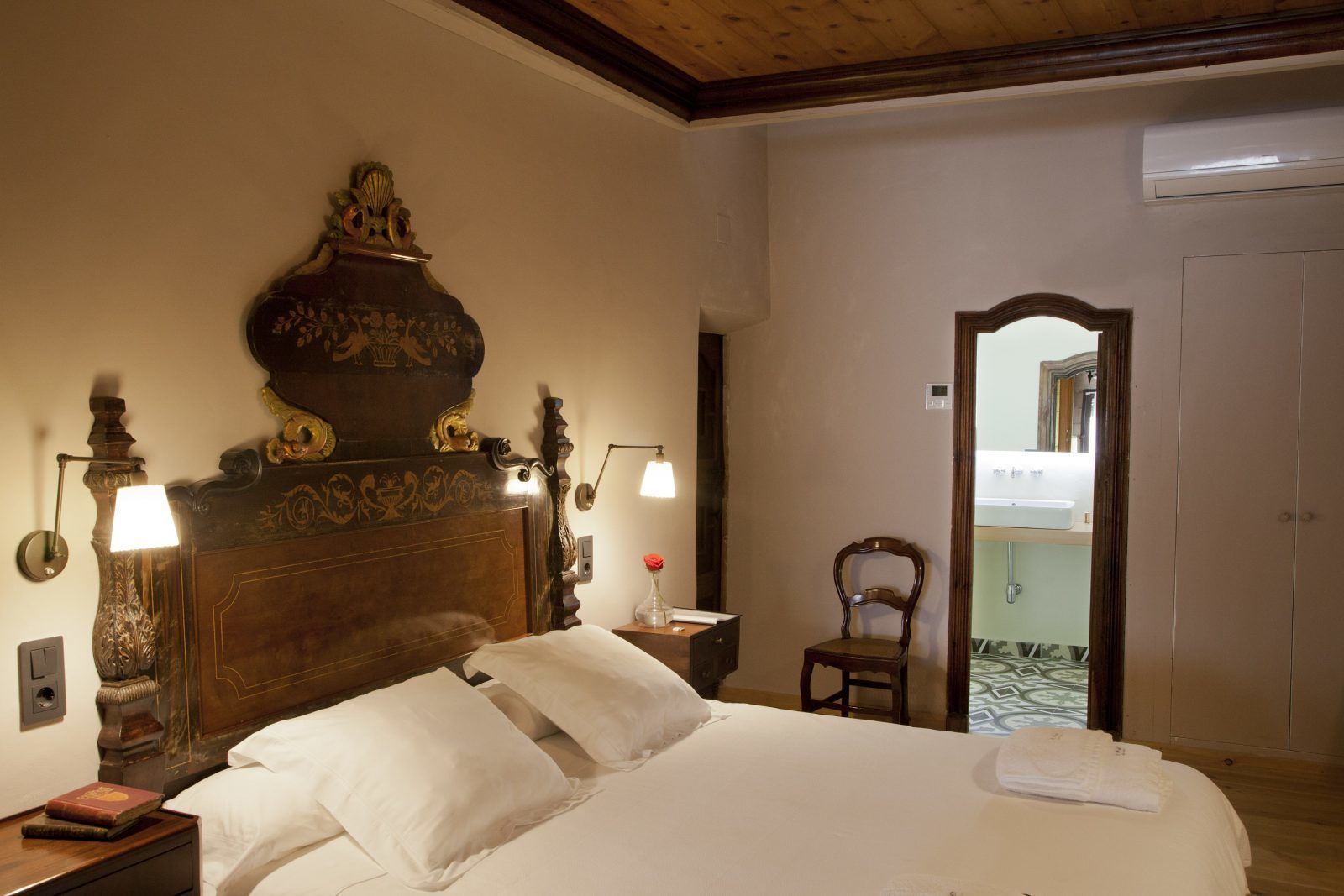 A hotel room with a large bed, a wooden headboard, two bedside lamps, a nightstand, a chair, and a mirror.