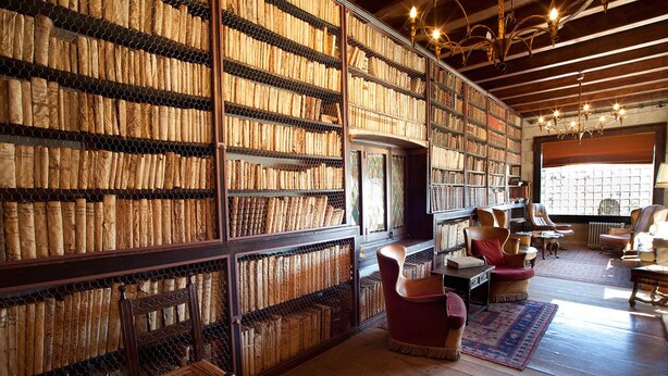Een bibliotheek met boekenplanken vol boeken, houten vloeren en lederen fauteuils.