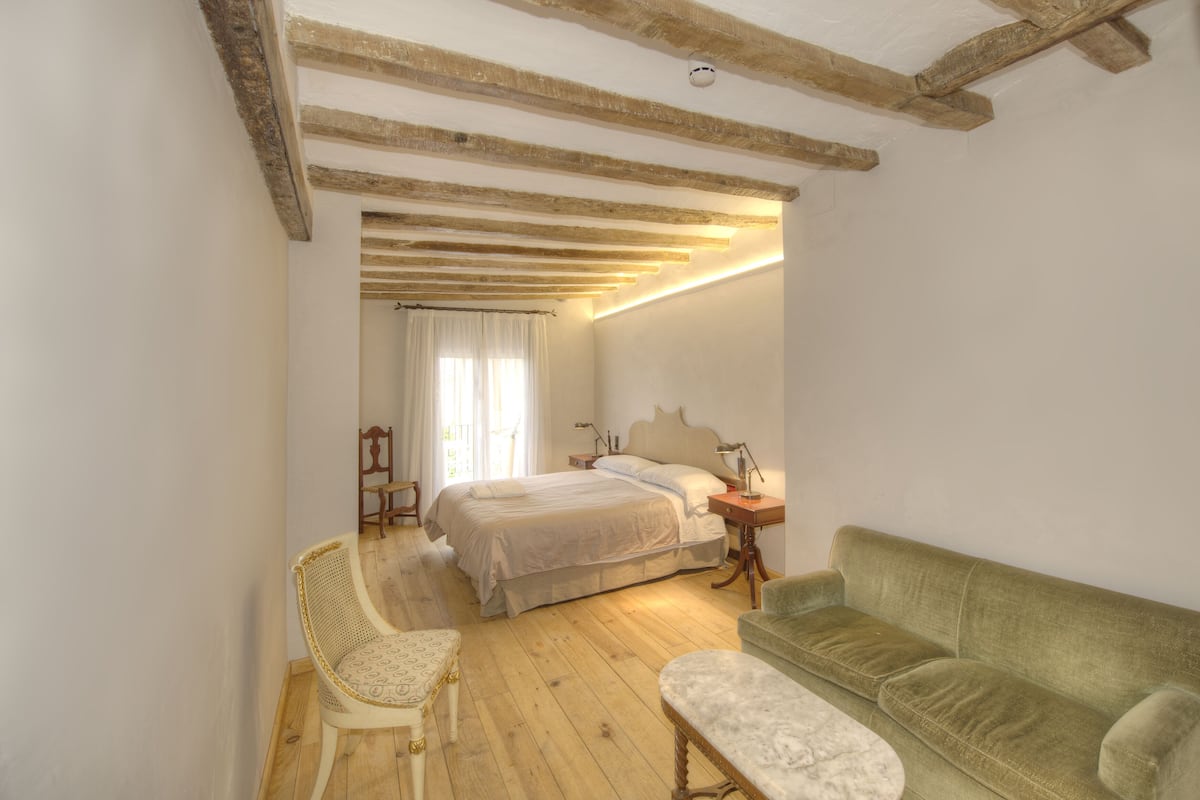 Une chambre à coucher avec un lit, un canapé vert, une chaise en bois, une table de chevet et une commode.