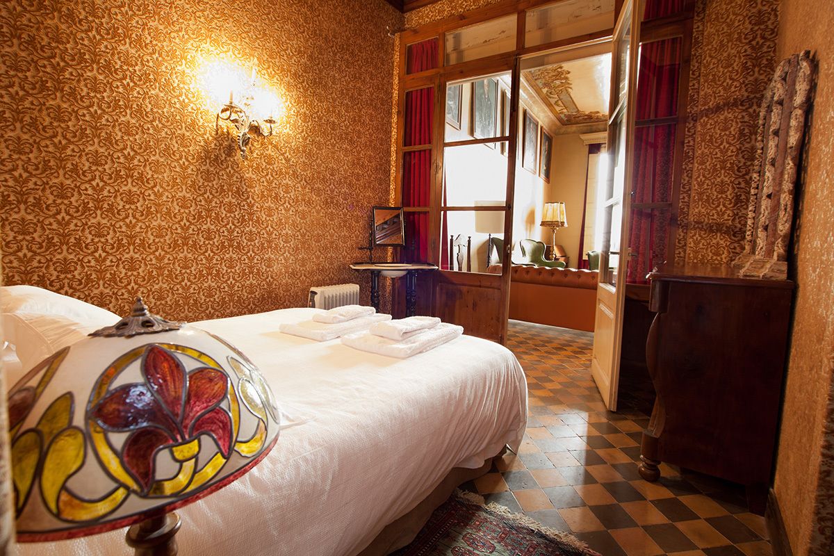 Habitación de hotel con una cama grande, una araña de cristal, un aparador de madera y vistas a la calle a través de una ventana.